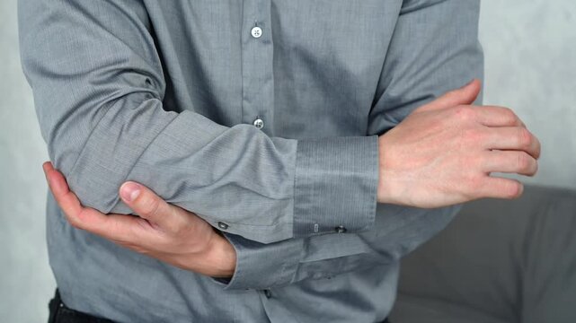 Man indoors feeling discomfort in his elbow while touching his arm, suggesting joint pain from repetitive movement or sports activity.