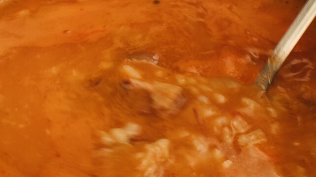 kharcho soup boiling and cooking close up, hot pot with greens rice and spoon spinning in a circle, georrgian restaurant, tomato soup macro. 