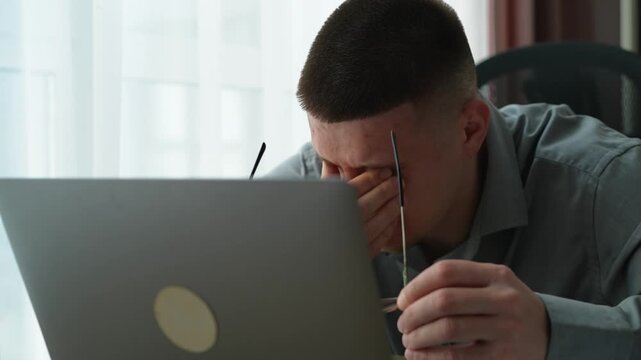 Close-up of a young male taking off glasses and massaging tired eyes after prolonged computer use. Concept of digital eye strain and work overload.