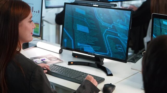 Smiling female software developer working on computer in office. Professional woman coder analyzing digital data and programming on screen. High tech corporate workspace for IT and cyber security