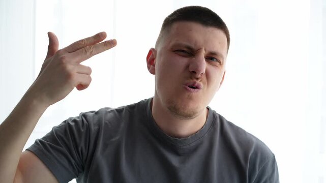 Man gesturing a finger gun to his temple in a humorous way, expressing overload and tiredness from work or daily tasks. Indoor lifestyle scene.