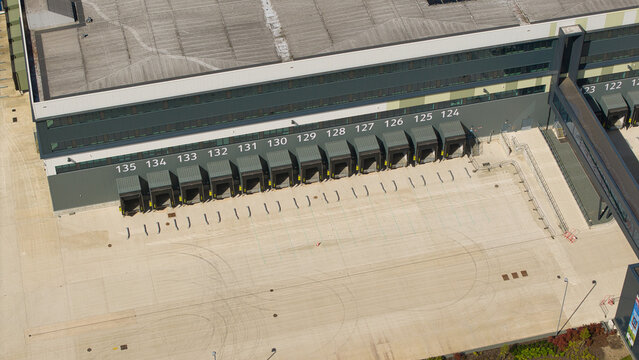 Aerial view of a supermarket distribution centre featuring numbered loading bays and a large concrete yard under bright sunlight in Nailstone, Nuneaton, United Kingdom.