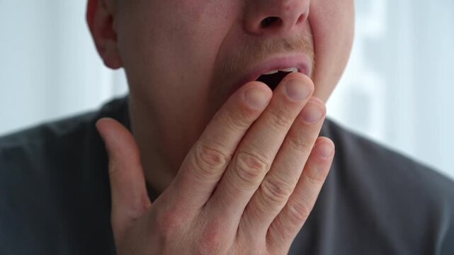 Close-up portrait of a sleepy young male yawning indoors, expressing morning fatigue and natural human reaction after waking up.