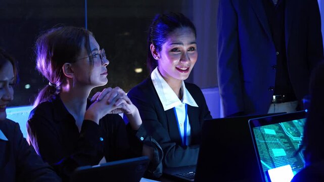 Professional business women analyzing software program and network security data on laptop during night office meeting, diverse colleagues discussing technical IT solutions and corporate strategy