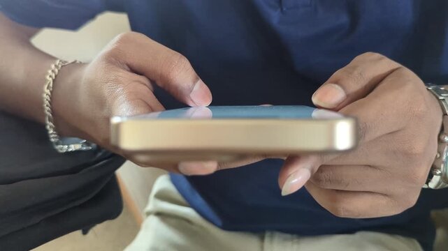 Close up view of persons hands typing on smartphone with gold frame and metal watch on wrist while sitting in casual indoor setting using mobile application for communication or business tasks.
