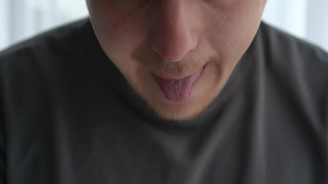 Close-up of a young man licking his lips, showing slightly dry skin, suggesting dehydration or need for lip care. Concept of natural body response and personal care.