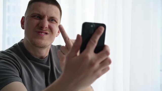 Young man during a smartphone video call making an offensive hand gesture toward the screen, expressing anger and conflict in online communication. 