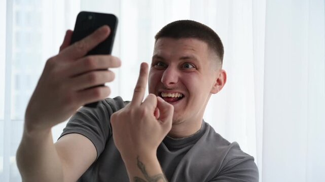 Man using a mobile phone for a video chat while displaying an insulting hand gesture, symbolizing conflict, rejection, and negative emotional response.