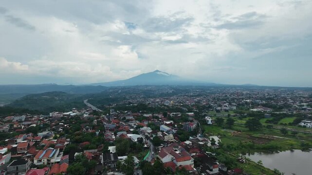 Aerial view of a suburban city with a majestic mountain in the background under cloudy skies.