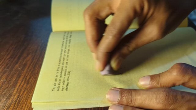 Hand erasing handwritten word money from yellow book page demonstrating concept of financial freedom and letting go of material obsession, close-up shot with focus on action and effort.