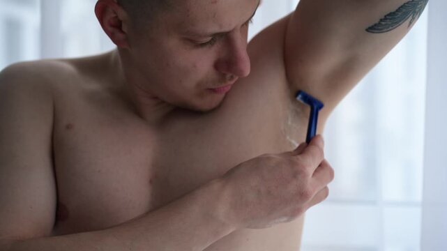 Close-up shot of a male shaving armpit hair with a razor under running water in the shower. Emphasis on grooming routine, odor control, and personal hygiene care.