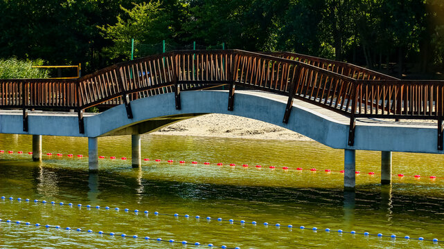 Curved wooden footbridge over lake with reflections in Pobiedziska Poland