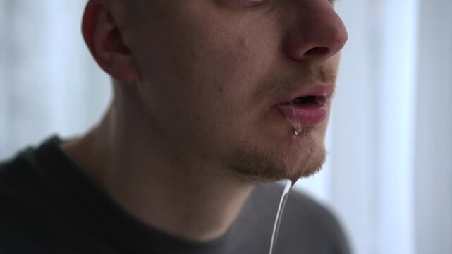 Young man in shock with water or saliva dripping from his mouth, showing a distressed facial expression in a close-up indoor scene. Concept of sudden illness, dehydration, or physical discomfort.