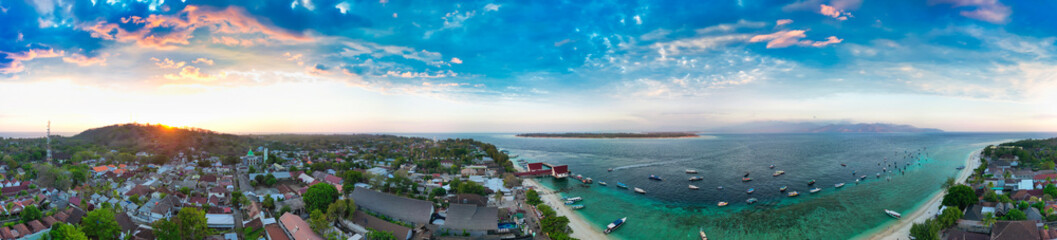 Fototapeta premium Aerial drone view of Gili Trawangan island at sunset showing golden sky, Mount Agung silhouette, and turquoise waters Indonesia