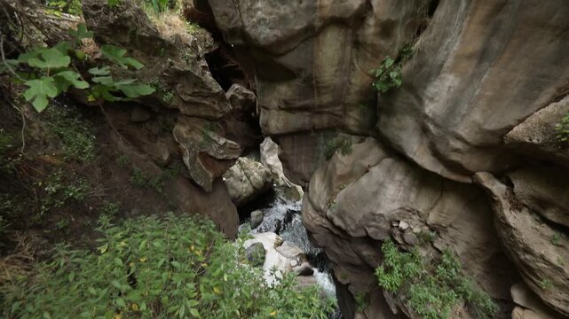The video begins with a close-up of a highly textured porous rock overhang. The camera then slowly tilts upwards revealing a steep, rugged cliff face with green vegetation.

