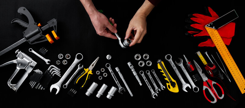 Top view of hands using a ratchet tool among a wide assortment of professional tools on a black background. Concept of repair, maintenance, construction and DIY work.