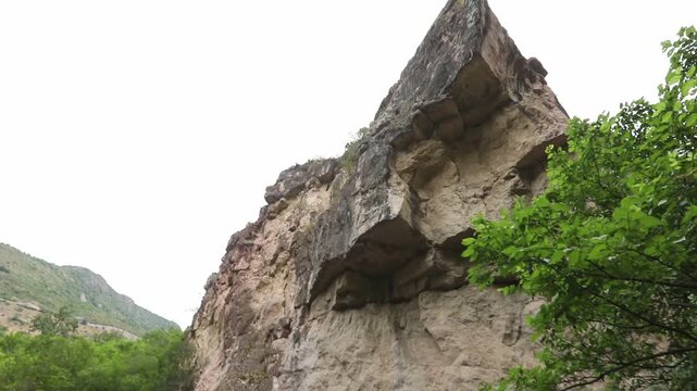 The video begins with a close-up of a highly textured porous rock overhang. The camera then slowly tilts upwards revealing a steep, rugged cliff face with green vegetation.

