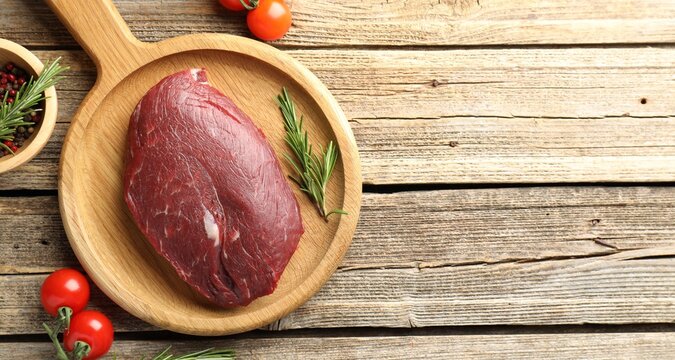 Raw beef steak, tomatoes and rosemary on wooden table, flat lay. Space for text
