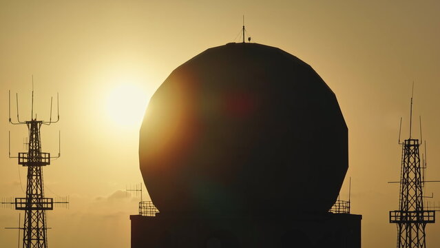 Silhouetted doppler radar and communication antennas rising against a vibrant sunset, highlighting the contrast between technology and nature