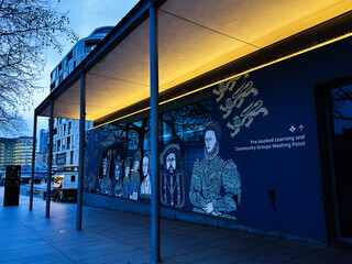 Naklejka premium Evening entrance mural at a London, UK learning and community meeting point with historic royal portraits and modern architecture under warm canopy lighting