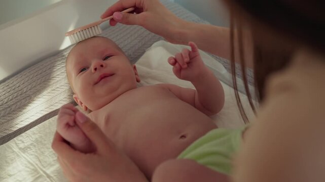 Mother gently brushes newborn baby hair with soft brush on changing table close up tender moment. Infant child family love parenthood cozy home adorable childhood innocence peaceful calm nurturing