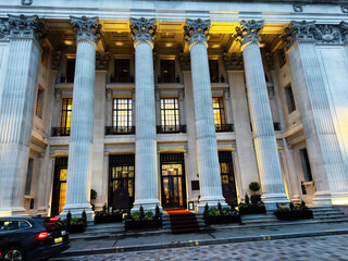 Naklejka premium Grand neoclassical building with Corinthian columns and illuminated hotel entrance in London UK at dusk on a city street. Four Seasons Hotel London at Ten Trinity Square.