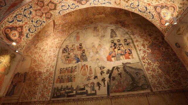 Slow pan inside an ancient church revealing an ornate interior. The walls and vaulted ceilings are beautifully adorned with vibrant religious frescoes, intricate murals, and elaborate decorative patte