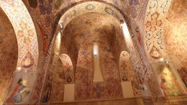 Slow pan inside an ancient church revealing an ornate interior. The walls and vaulted ceilings are beautifully adorned with vibrant religious frescoes, intricate murals, and elaborate decorative patte