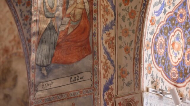 Slow pan inside an ancient church revealing an ornate interior. The walls and vaulted ceilings are beautifully adorned with vibrant religious frescoes, intricate murals, and elaborate decorative patte