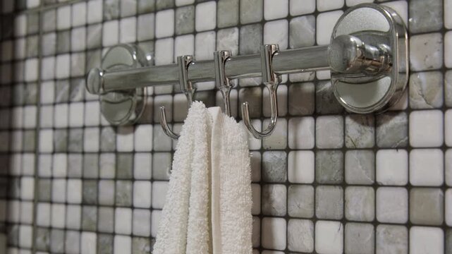 Woman hand hanging towel on hook on towel holder on wall in bathroom