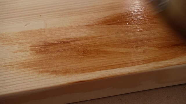 Brush spreads fresh stain along wooden edge during indoor renovation work.