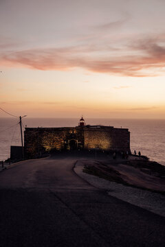 Coastal fortress with lighthouse at Nazare Portugal in warm photographic style on sunset backdrop, concept of travel and heritage