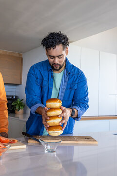 Friends holding stack of four glossy burger buns while preparing meal on modern kitchen counter