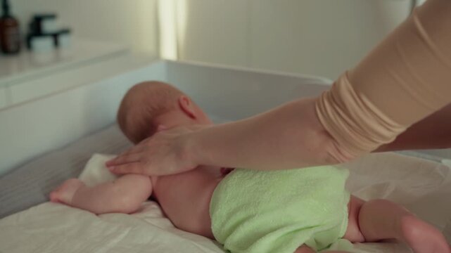 Parent gently massages newborn baby back and legs on changing table with soft towel lotion bottles background promoting bonding relaxation hygiene and comfort. Infant child family love parenthood cozy