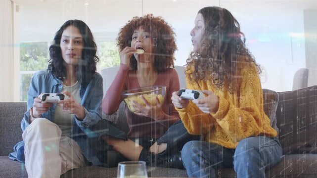 Three women gaming on couch, pressing pads with HUD overlaying screen, snacking chips, competing