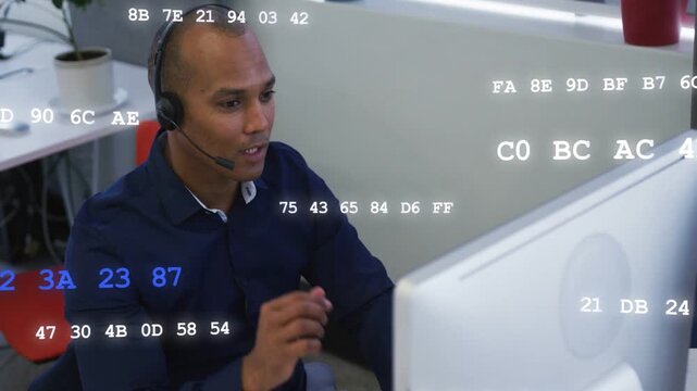 Mid-adult man receiving support call at desk, adjusting mic while hex codes scrolling on monitor