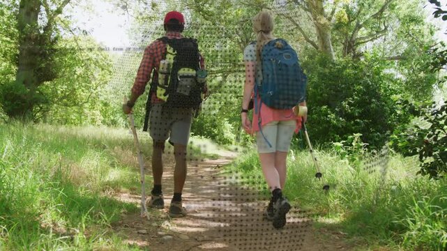 Camera starting behind pair walking with packs and poles toward sunlit glade, dot overlay appearing