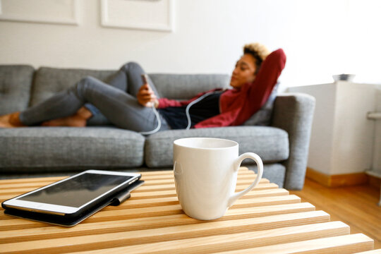 Young woman relaxing on couch with smartphone and coffee table in foreground