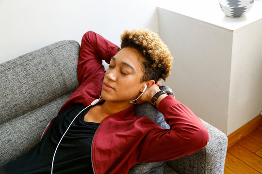 Young woman relaxing on sofa with headphones and eyes closed at home