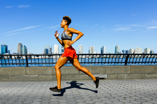 Athletic woman running along waterfront in New York City on sunny day