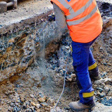 Construction worker using jackhammer at excavation site