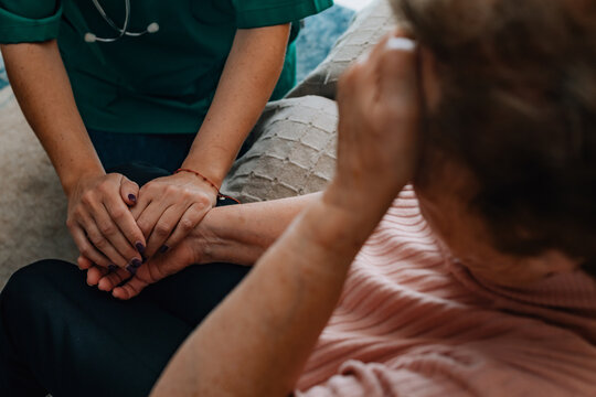 Home Healthcare_A healthcare professional in scrubs tenderly holds an elderly patient's hand at home, conveying empathy, trust, and the human connection at the heart of caregiving