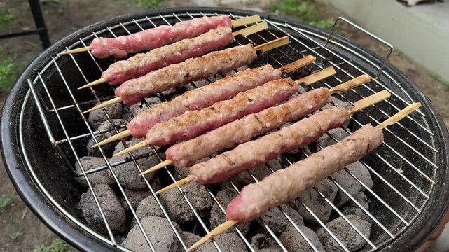 Skewered minced meat kebabs grilling over charcoal on a round barbecue, outdoor backyard cooking scene with smoky heat and casual summer gathering mood