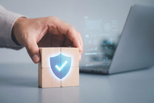 Hand placing wooden blocks with shield icon near laptop for cybersecurity and data protection concept
