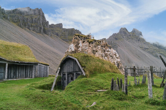 Old turf house stands near rocky mountains in Iceland on a clear day with blue sky