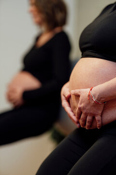 Two pregnant women seated indoors, natural photo style, on neutral background, concept of motherhood and care