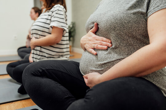 Pregnant women seated in calm indoor setting during a natural-light photo session on mats, concept of prenatal wellness