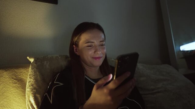 Girl doom scrolling her smartphone on a coach at night. Social network and phone addiction concept. Cozy home ambient light