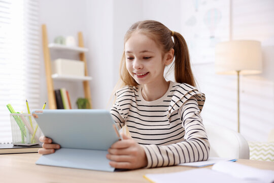 Cute girl with tablet doing homework at table indoors