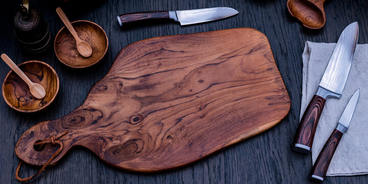 Wooden cutting board and knives displayed on a rustic table with wooden bowls and spoons for kitchen preparation